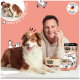 Braun-weißer Hund mit Person, die DOGS'n TIGER Schüssel und Produktbox hält, 'Made in Germany'-Abzeichen auf rosa Hintergrund.