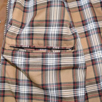 Nahaufnahme einer beigen karierten Haustierjacke mit schwarzen, weißen und roten Streifen und einer kleinen Reißverschlusstasche.