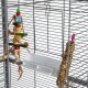 Buntes Holzspielzeug für Vögel, das in einem Haustierkäfig hängt, mit einem Saatenstick-Leckerli und einem weißen Futternapf darunter.