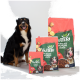 Schwarz-brauner Hund neben drei rot-grünen VUTTER!-Hundefuttertüten mit der Aufschrift 'Pflanzlich Vollwertig Lecker'.
