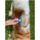 Eine Person verwendet eine blaue Bürste zur Fellpflege an einem flauschigen Hund mit einer Mischung aus weißem und braunem Fell, vor einem grünen Hintergrund.