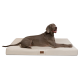 Ein glücklicher grauer Hund liegt auf einem großen, cremefarbenen Hundebett mit einem braunen Logoetikett.