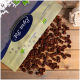 Eine Tüte mit Tierleckerlis mit der Aufschrift "Paw Pet" und einem blauen Logo, die kleine, quadratische, braune Leckerlis auf eine Holzoberfläche fallen lässt.