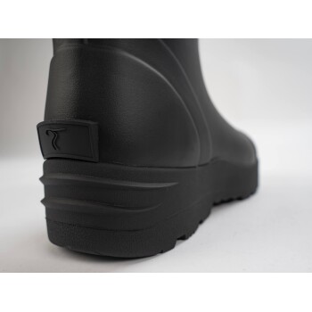 Nahaufnahme der Rückseite eines schwarzen Gummistiefels, mit einer strukturierten Oberfläche und einem kleinen Logo an der Ferse.