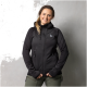 Eine Person in einer schwarzen Zip-Jacke mit Kapuze, mit einem kleinen Logo auf der Brust, steht vor einem grauen Hintergrund.