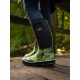 Eine Nahaufnahme einer Person, die lebhaft grüne und schwarze gemusterte Gummistiefel trägt, die auf einer Holzoberfläche in einem bewaldeten Gebiet steht.