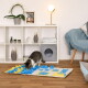 Getigerte Katze schnüffelt an einer blau-gelben Snuffle-Matte auf dem Boden in einem modernen Wohnzimmer mit weißem Würfelregal und grauem Katzenwürfel.