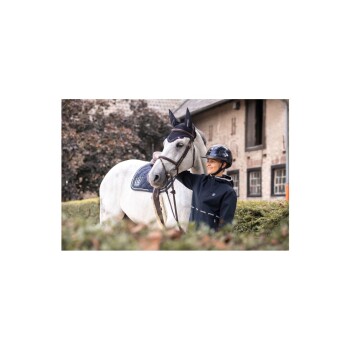 Ein Reiter in einer schwarzen Jacke hält sanft die Zügel eines weißen Pferdes, das ein marineblaues Sattelpad trägt, in einer üppigen Außenumgebung.