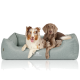 Zwei Hunde liegen zusammen in einem gemütlichen, hellgrauen Hundebett, mit dem Logo "KNUFFELWUFF" auf der Vorderseite sichtbar.