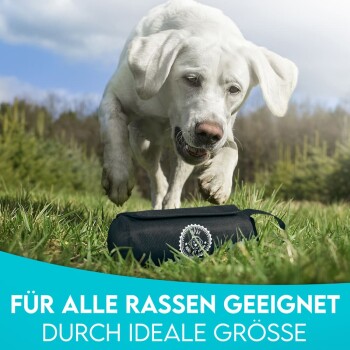 Ein verspielter weißer Hund steht auf Gras neben einer schwarzen Haustierzubehörtasche, mit dem Text darunter, der besagt "FÜR ALLE RASSEN GEEIGNET DURCH IDEALE GRÖSSE."