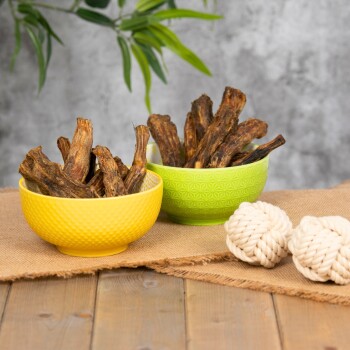 Zwei bunte Schalen gefüllt mit Hundekauartikeln, eine gelbe und eine grüne, auf einer Juteschnur neben zwei weißen Seilspielzeugen platziert.