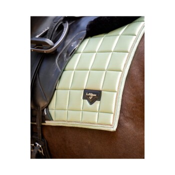 Nahaufnahme eines hellgrünen, gesteppten Sattels mit einem schwarzen LeMieux-Logo, auf der Seite eines braunen Pferdes platziert, das Reitzubehör zeigt.