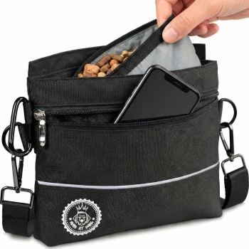 Eine Hand, die ein Hundeleckerli in eine schwarze Hundeleckerli-Tasche mit Reißverschluss und einem Logo steckt, mit einem Schultergurt und reflektierenden Details.