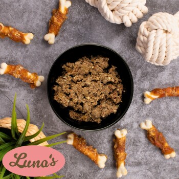 Schüssel mit Haustierfutter umgeben von Hundeleckerlis und Seilspielzeugen, mit "Luna's" Logo in Pink in der unteren linken Ecke.