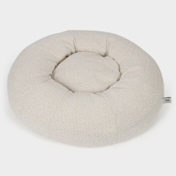Rundes, plüschiges Hundebett in hellbeige mit einem gepolsterten Design, mit einem kleinen "Paw Wow"-Tag an der Seite.