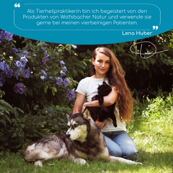 Frau im Garten hält eine schwarze Katze, ein großer Hund steht neben ihr; oben deutsches Testimonial mit Bezug auf Wolfsbacher Natur.