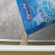 Eine Tüte Lyra Pet Power Ultra Katzenstreu wird in eine weiße Katzentoilette gegossen, mit einem strukturierten grauen Hintergrund.