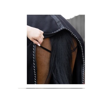 Eine Nahaufnahme einer Hand, die eine schwarze Pferde-Decke zurückzieht und das braune Fell und den langen schwarzen Schwanz des Pferdes zeigt.