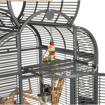 Eine Nahaufnahme eines grauen Vogelkäfigs mit einem hängenden Spielzeug mit bunten Blöcken, einer Futterschale und einer natürlichen Holzstange.