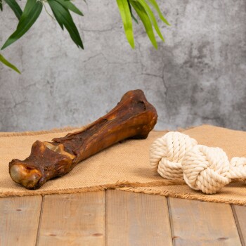 Ein Hundekau-Knochen und ein geknotetes Seilspielzeug werden auf einer Juteschicht präsentiert, mit einem strukturierten grauen Hintergrund und einer Holzoberfläche.