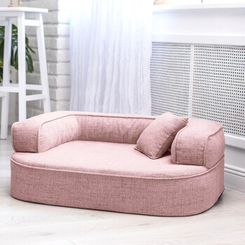 Ein schwarzer und brauner Dackel liegt bequem auf einem weichen rosa Haustierbett mit zwei kleinen Kissen, in einem hellen, luftigen Raum.