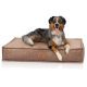 Ein glücklicher Australian Shepherd Hund mit einem blauen Merle-Fell liegt auf einem plüschigen, braunen Cord-Hundebett und zeigt ein Lederetikett.