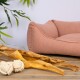 Ein gemütliches, pinkes Haustierbett mit weichen, abgerundeten Kanten, umgeben von grünen Blättern und einem Holzsockel, ideal für kleine Haustiere.