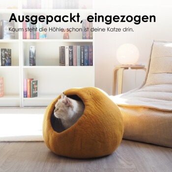 Gemütliches graues Haustierbett mit runder Form und kleinem Eingang, auf einer weißen Decke mit grünen Pflanzen. Text: "Perfekter Rückzugsort."