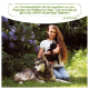 Eine Frau hält eine schwarze Katze, während sie neben einem sibirischen Husky in einem Garten mit lila Blumen sitzt. Textzitat von Lena Huber über Haustierprodukte.