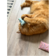 Un chat orange roule joyeusement sur le sol, tenant un petit jouet en tissu coloré à pois dans ses pattes.