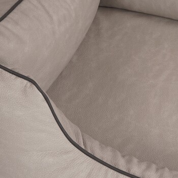 Eine Nahaufnahme eines weichen, beigen Haustierbettes mit einer strukturierten Oberfläche und schwarzer Paspelierung entlang der Kanten.