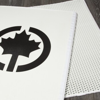 Schwarz-weiße Haustiermatte mit einem stilisierten Ahornblatt-Logo, auf einer strukturierten weißen Oberfläche platziert.