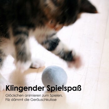 Eine verspielte Katze, die mit einem grauen Filzball auf einem Holzboden spielt, mit einem Text darunter, der "Klingender Spielspaß" und eine Beschreibung der Eigenschaften des Spielzeugs liest.