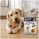 Gelber Labrador kaut an einem Fleisch-Snackstreifen auf dem Boden neben einer Tüte mit der Aufschrift 'PREMIERE. I ♥ my dog' und 'Meat Snack strips'.