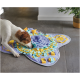 Petit chien brun et blanc reniflant un tapis de recherche de nourriture violet, sarcelle et jaune sur un sol carrelé gris.