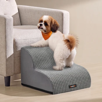 Kleiner weiß-brauner Hund mit orangefarbener Bandana auf einer grauen, strukturierten Haustier-Rampe mit dem Label 'Feandrea' neben einem beigefarbenen Sessel.