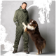 Eine Person in einem olivgrünen Overall steht neben einem verspielten braun-weißen Australian Shepherd, beide lächeln.