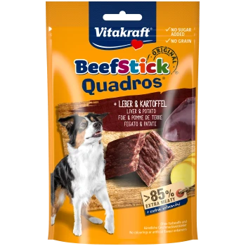 Vitakraft BeefStick Quadros Hundeleckerlis Verpackung mit einem Hund, mit Text, der "Kein Zucker hinzugefügt", "Kein Getreide" und "85 % extra fleischig" hervorhebt.