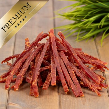 Haustierleckerlis in Premiumqualität in langen, dünnen Streifen, auf einem Holzuntergrund in einem Haufen angeordnet, mit grünem Gras im Hintergrund.