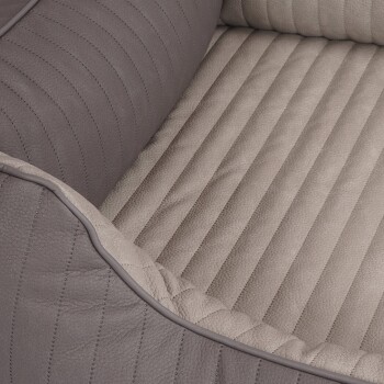 Eine Nahaufnahme eines Haustierbettes mit einem grauen Lederäußeren mit vertikaler Naht und einem weichen beigen Innenraum mit gerippter Textur.