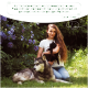 Eine Frau mit einer schwarzen Katze sitzt neben einem sibirischen Husky, umgeben von lila Blumen. Text: "Als Tierheilerin liebe ich die Produkte von Wolfsbacher Natur."