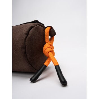 Eine Nahaufnahme einer braunen Haustierspielzeugtasche mit einem orangefarbenen Kordelzug und schwarzen Spitzen, vor einem weißen Hintergrund.