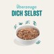 Schüssel mit Haustierfutter, das eine strukturierte Mischung und kleine Gemüsestücke enthält, begleitet von dem Text "Überzeuge DICH SELBST" darüber.