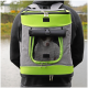 Eine Person trägt einen grauen und grünen Haustiertrage-Rucksack mit einem Netz vorne, der einen kleinen Hund zeigt, in der Nähe eines Gewässers.