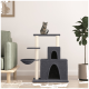 Ein grauer Katzenbaum mit mehreren Ebenen, mit einem gemütlichen Versteck, Kratzpfosten und einer hängenden Schüssel, mit einer getigerten Katze, die oben sitzt.