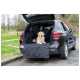 Ein Golden Retriever sitzt auf einer schwarzen Haustier-Sitzauflage im Kofferraum eines schwarzen SUVs, der auf einer Grasfläche geparkt ist.
