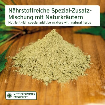 Grüner Kräuterpulverhaufen auf Holz, Etikett: ‚Nährstoffreiche Spezial‑Zusatz‑Mischung‘.