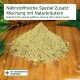 Grüner Kräuterpulverhaufen auf Holz, Etikett: ‚Nährstoffreiche Spezial‑Zusatz‑Mischung‘.