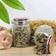 Zwei Glasgefäße mit braunen Tierpellets, eines aufrecht und eines verschüttet auf einem Tisch, mit Heu, einem Salzleckstein und grünen Blättern