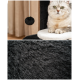 Eine flauschige graue Katze sitzt auf einer weißen Plattform eines schwarzen Katzenbaums, mit einem hängenden schwarzen Pom-Pom-Spielzeug darüber.